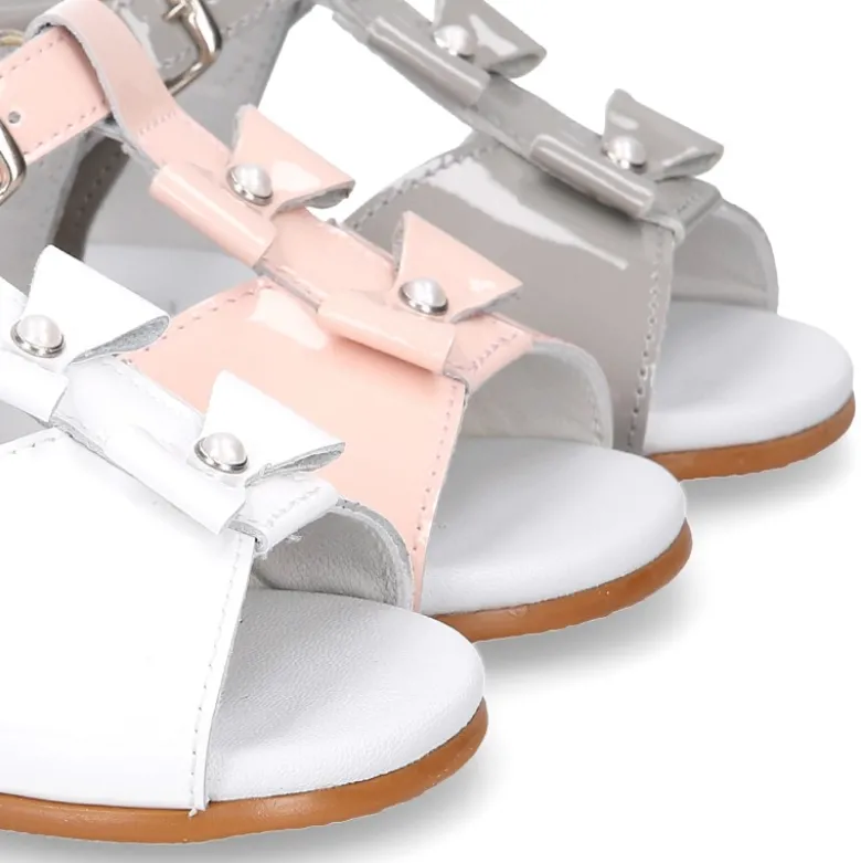 Sandalia peques en forma de T con dos lazos y perlas en piel charol.