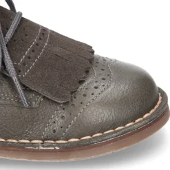 Zapatito tipo blucher con lengüeta con flecos y picados en piel combinada.